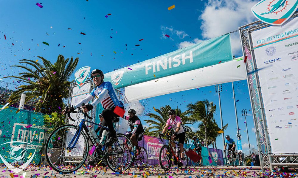 Chris Fitzmaurice riding a bike across the finish line at the Miami Dolphin's Cancer Challenge in Miami 